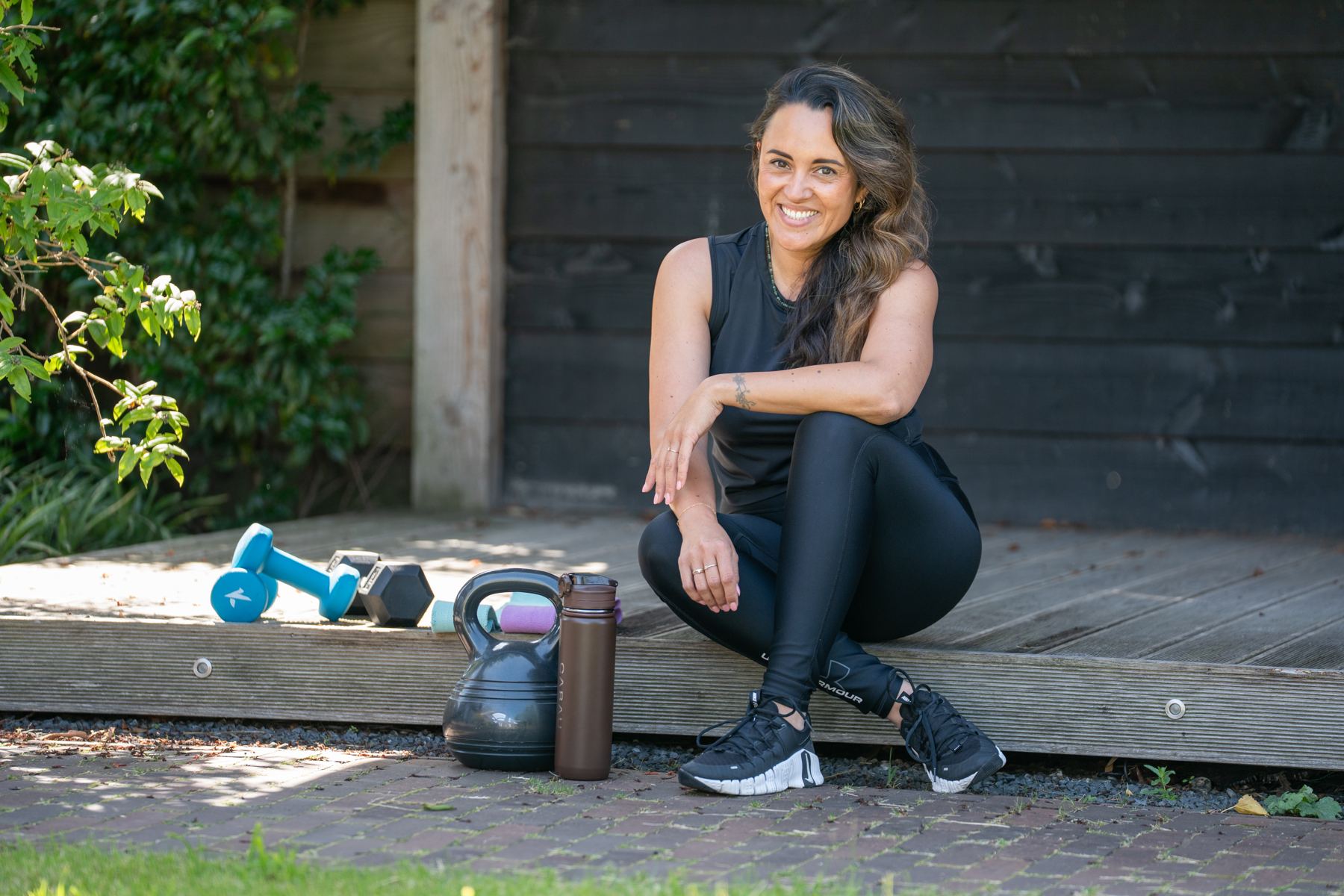 Romy in sportkleding op een houten vlonder naast kettlebells en dumbbells