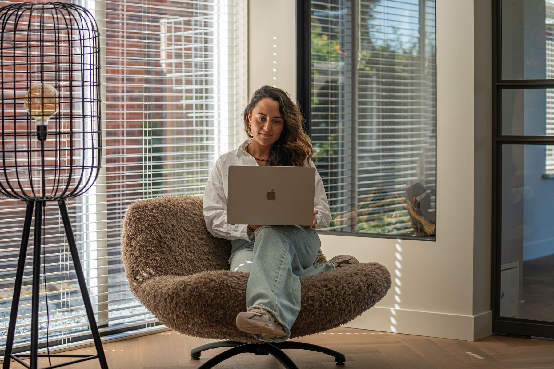Romy werkt op een laptop in een fauteuil bij het raam