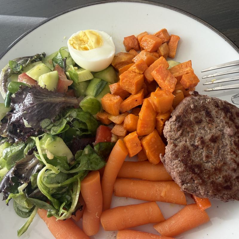 Plate with salad, boiled egg, sweet potato, carrot and a burger