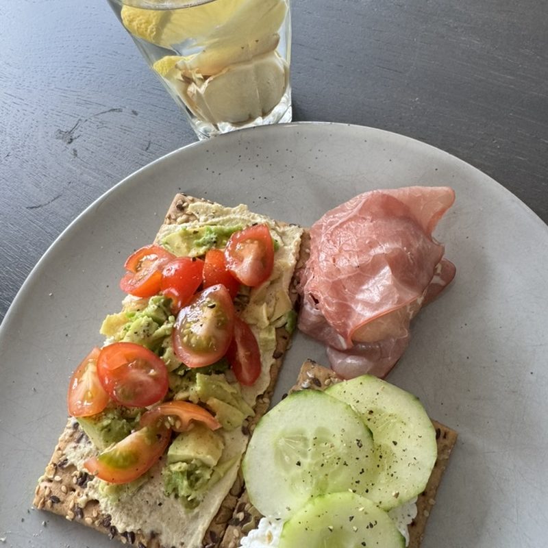 Crackers with avocado, tomato and cottage cheese, cucumber and a glass of water with lemon